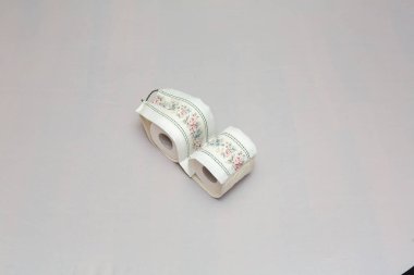 Çiçekli kumaşla kaplı iki rulo tuvalet kağıdı masaya oturur ve zarafet katar.