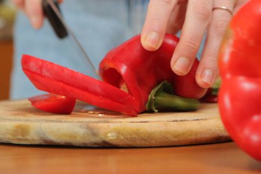 Ahşap kesme tahtasında taze kırmızı dolma biber dilimleyen şefin yakın çekimi, sağlıklı yemek için malzemeler hazırlamak.