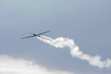 Küçük uçak akrobatik manevralar yaparak mavi gökyüzüne doğru beyaz bir duman izi bırakıyor.