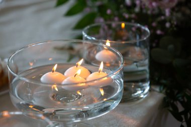 Cam kâselerde yanan yuvarlak, beyaz yüzen mumlar dekore edilmiş masa düzenine biraz romantizm katıyor.