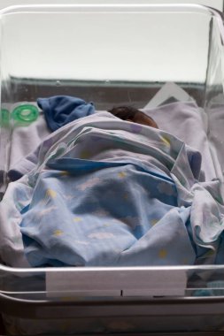 Yeni doğmuş bebek, hastane beşiğinde huzur içinde uyuyor. Bulutlar ve yıldızlarla kaplı mavi bir battaniyeye sarılı.