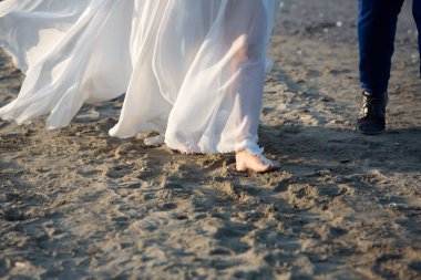 Yeni evliler gün batımında sahilde çıplak ayakla yürürken karı koca olarak ilk anlarının tadını çıkarıyorlar.