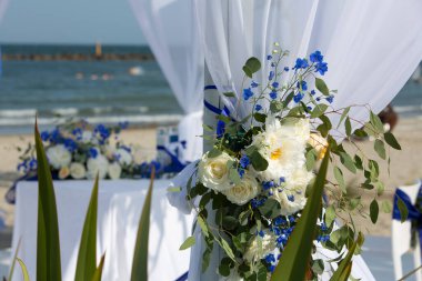 Güzel beyaz ve mavi çiçek aranjmanı güneşli bir sahilde düğün çardağı süslüyor.