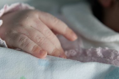 Yeni doğan bebeğin narin eli yumuşak bir battaniyeye uzanır. Minik parmakları ve yeni hayatın saf masumiyetini sergiler.