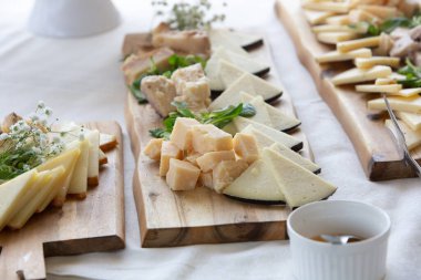 Peynir tabağı çeşitli peynirler sunuyor, balla servis ediliyor, ahşap kesim tahtalarında servis ediliyor.