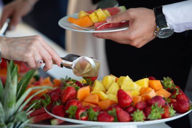Garson ananas, karpuz, kavun ve çilek içeren bir tabak taze meyve salatası servis ediyor.