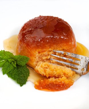 Altın şuruplu haşlanmış puding, sade beyaz tabakta tek porsiyon.