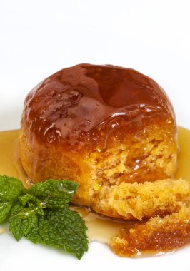 Altın şuruplu haşlanmış puding, sade beyaz tabakta tek porsiyon.