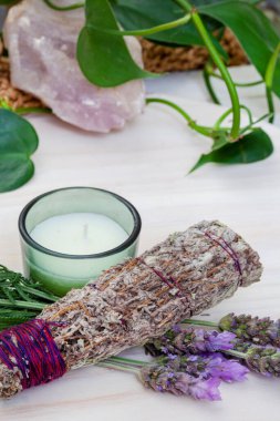 Smudge stick with candle and lavender on a table with plants and crystals