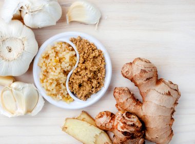 garlic and ginger, whole and crushed flat lay on light wood
