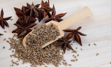 Aniseed and pods on light wooden surface with wooden scoop