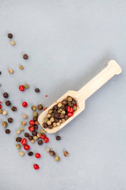 mixed whole peppercorns on a grey surface with wooden scoop