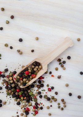 mixed whole peppercorns on a light wooden surface with a wooden scoop