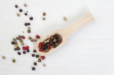 mixed whole peppercorns on a light wooden surface with a wooden scoop