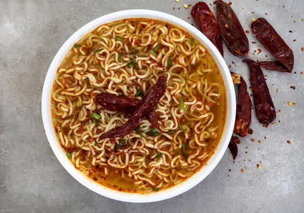 spicy instant noodles or ramen with dried chili on mottled grey with copy space. Flat lay, top view