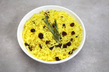 Geleneksel Güney Afrika sarı pirinci, zerdeçal ve biberiye garnitürlü kuru üzümler, benekli gri yüzey üzerinde yuvarlak kase 