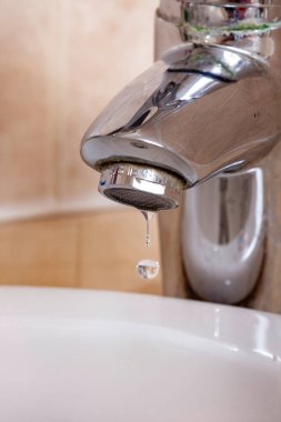 Lavaboya su damlatan bir musluk. Su berrak ve musluk gümüş.