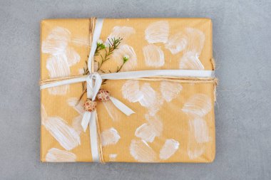 Çevre dostu hediye paketleme fikirleri. Beyaz fırça darbeleriyle süslenmiş düz kahverengi kağıda sarılmış bir hediye ve biraz kurdele, boncuk ve çiçek dalı.