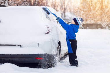 Küçük çocuk aile arabasından kar temizlemeye yardım ediyor.