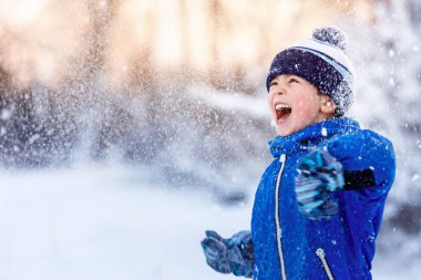 Mutlu küçük çocuk karda eğleniyor. Çocuklar için açık hava kış aktiviteleri. Çocuk karlı bir günde parkta yürümekten zevk alır.