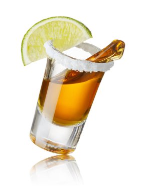 Düşen cam bardakta tekila, tuzlu ve limon dilimli beyaz arka planda izole edilmiş.