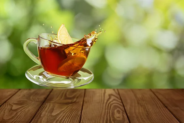 Fliegendes Glas Tee Mit Spritzer Und Fallender Zitronenscheibe Auf Holztisch Stockfoto