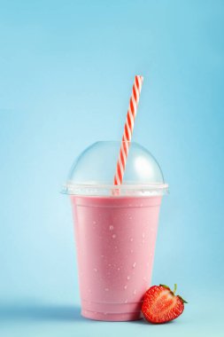Soğuk çilekli milkshake mavi arka planda samanla tek kullanımlık plastik bardakta.