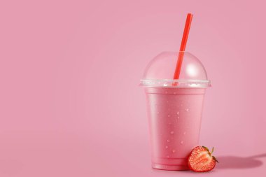 Tek kullanımlık plastik bardakta, pembe arka planda saman olan soğuk çilekli milkshake.