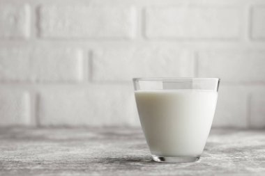 Arka planda beyaz tuğla duvar olan gri masanın üzerindeki camda süt
