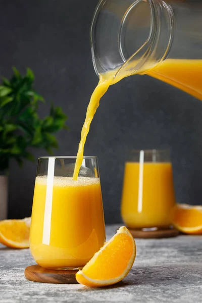 orange juice pouring into glass from jug on table with dark background