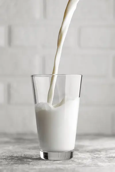 milk pouring in big glass on grey table with white brick wall as background