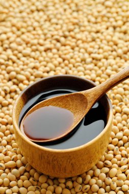 Ahşap kasede soya sosu ve arka planda kuru soya fasulyesi kaşığı.