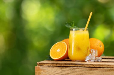 Bir bardak soğuk portakal suyu ya da buzlu yaz kokteyli ve arka planda yeşil bahçeli ahşap masa.
