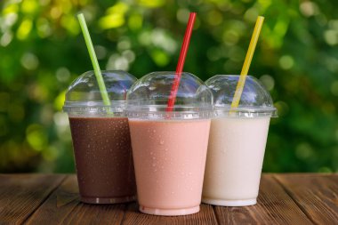Tek kullanımlık plastik bardaklarda, dışarıdaki ahşap masada samanla değişik lezzetli milkshake setleri.