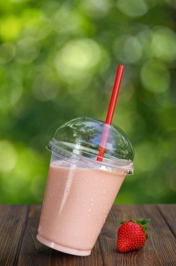 Eğri büğrü plastik bardak çilekli milkshake veya açık havada ahşap masada smoothie.