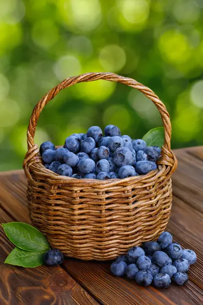 Stock image ripe big blueberries in wicker basket on wooden table outdoors