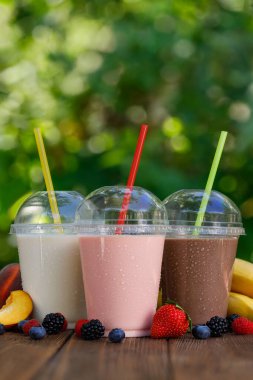 Farklı aromalı milkshake seti ya da tek kullanımlık plastik bardakta açık havada saman ve taze muz ve meyveli smoothie.