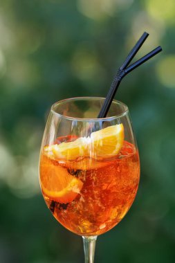 Yakın plan soğuk aperol sprey kokteyli. Yeşil doğal arka planda siyah pipetler.