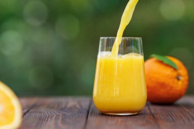 Arkaplanda yeşil bahçe olan ahşap masaya dökülen portakal suyu.