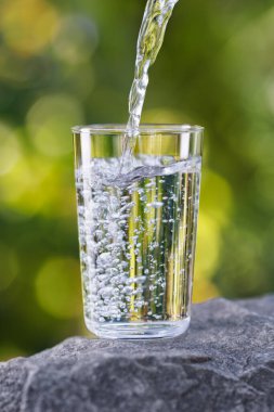 İçme suyu taşın üzerine dökülen yeşil doğal arkaplan.