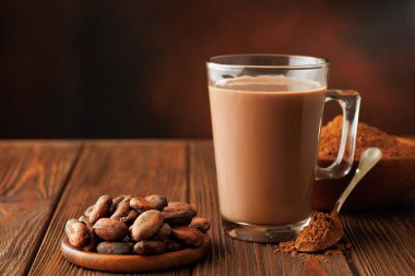 Cam bardakta sıcak çikolata ve tahta masada pudralı kakao fasulyesi.