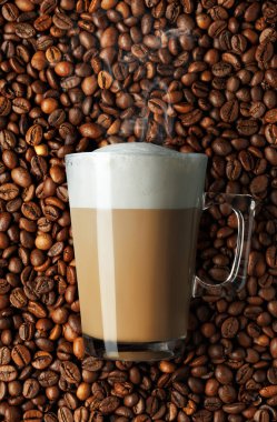 Kapuçino, cam bardakta kremşanti ve kahve çekirdekleri arka planda.