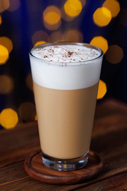 Bardakta kapuçino ve masada bokeh arkaplan serpiştirilmiş çikolata.