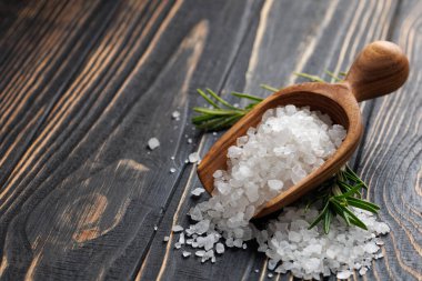 Kepçede beyaz deniz tuzu ve siyah ahşap masada yeşil biberiye.