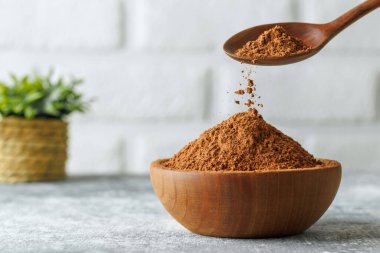 Masadaki tahta kaşıktan dökülen kakao tozu. Arka planda beyaz tuğla duvar var.