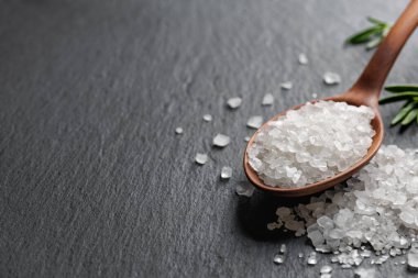 Tahta kaşıkta beyaz deniz tuzu ve siyah taş zemin üzerinde yeşil biberiye.