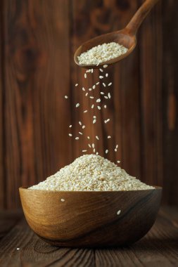 Tahta arka plandaki masada kaşıktan dökülen susam tohumları.