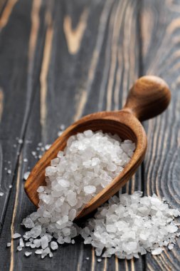 Koyu ahşap masada kepçedeki beyaz deniz tuzu