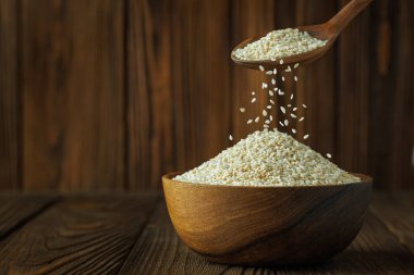 Tahta arka plandaki masada kaşıktan dökülen susam tohumları.