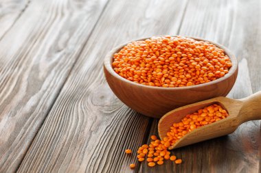Kırmızı mercimek ahşap bir kase ve kepçeyle dolup taşıyor, kırsal bir masada sıcak ve davetkar bir sahne yaratıyor, sağlıklı beslenme ve pişirme kavramlarını sergilemek için mükemmel.